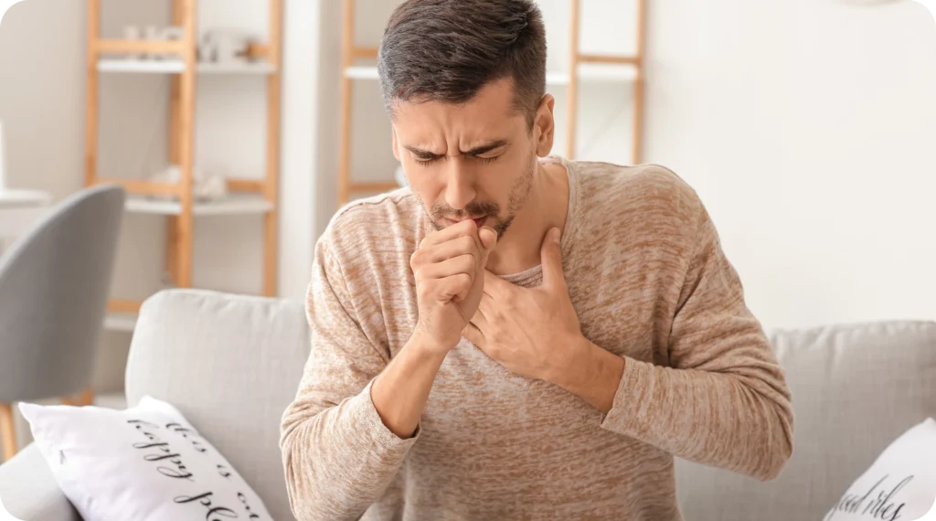 A man coughing while holding his chest, likely experiencing respiratory discomfort